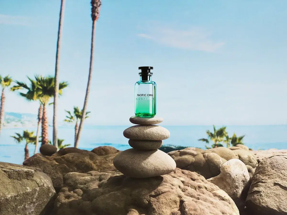 louis vuitton pacific chill edp campaign شیشه پسفیک چیل لویی ویتون روی سنگهای چیدهشده کنار ساحل و نخلها، در تصویر تبلیغاتی لویی ویتون