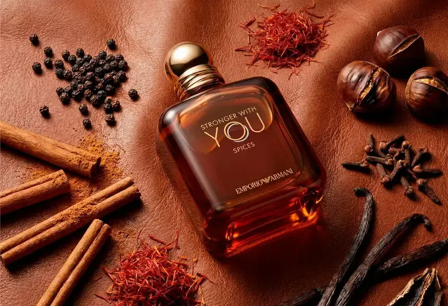 emporio armani stronger with you spices 100ml spices on leather flat lay بطری مسیرنگ عطر استرانگر ویت یو اسپایسز روی چرم، کنار فلفل سیاه، زعفران، چوب دارچین، میخک، شاهبلوط و غلاف وانیل