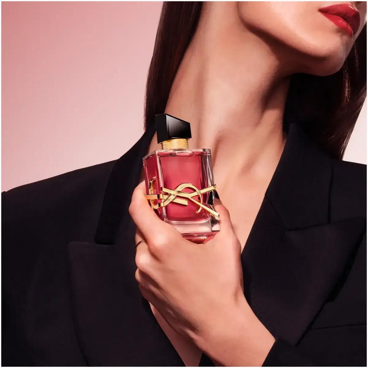 yves saint laurent libre berry crush campaign مدلی با کت مشکی و رژ لب قرمز، شیشهی لیبر بری کراش را کنار گردنش گرفته است؛ تصویر تبلیغاتی ایو سن لوران